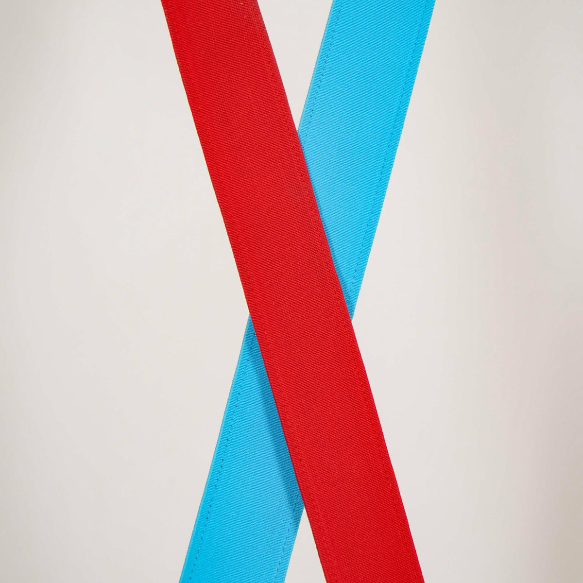 Close view of red and light blue woven webbing strips crossing on a Clérachic floor lamp, against a pale backdrop.