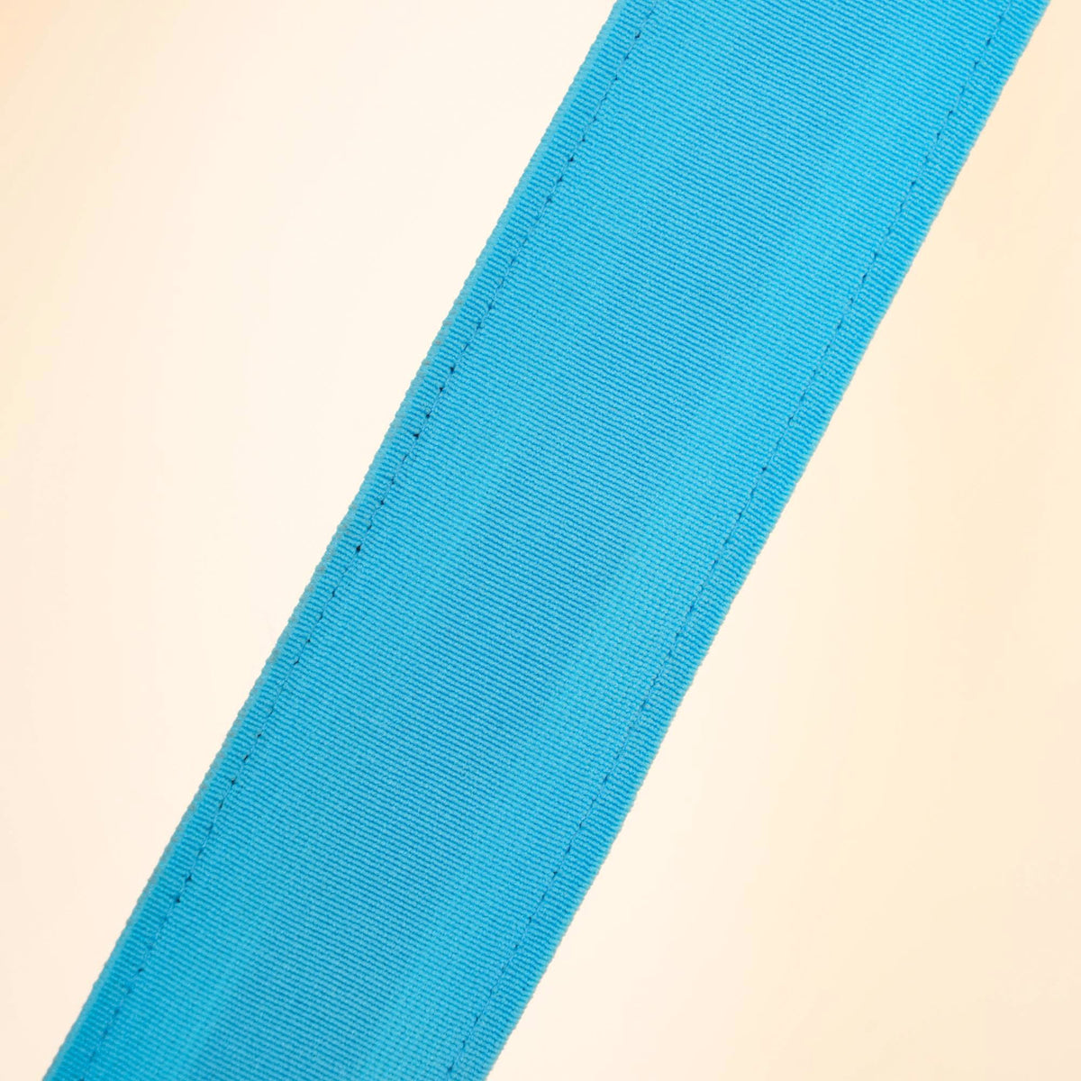 Close view of a light blue webbing strip of a Clérachic floor lamp, showing its fine ribbed weave and stitching on a cream backdrop.