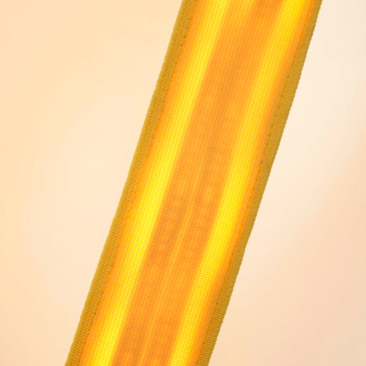 Close view of a lit yellow webbing strip on a Clérachic floor lamp, the warm light glowing through the woven fabric.