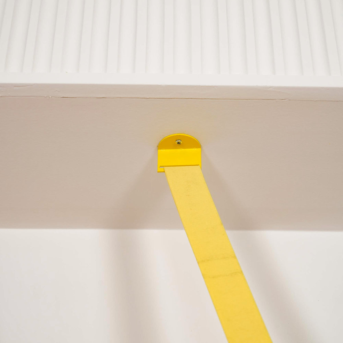 A small yellow metal plate and screw fix the top of this Clérachic floor lamp strip to the underside of a white ceiling beam.