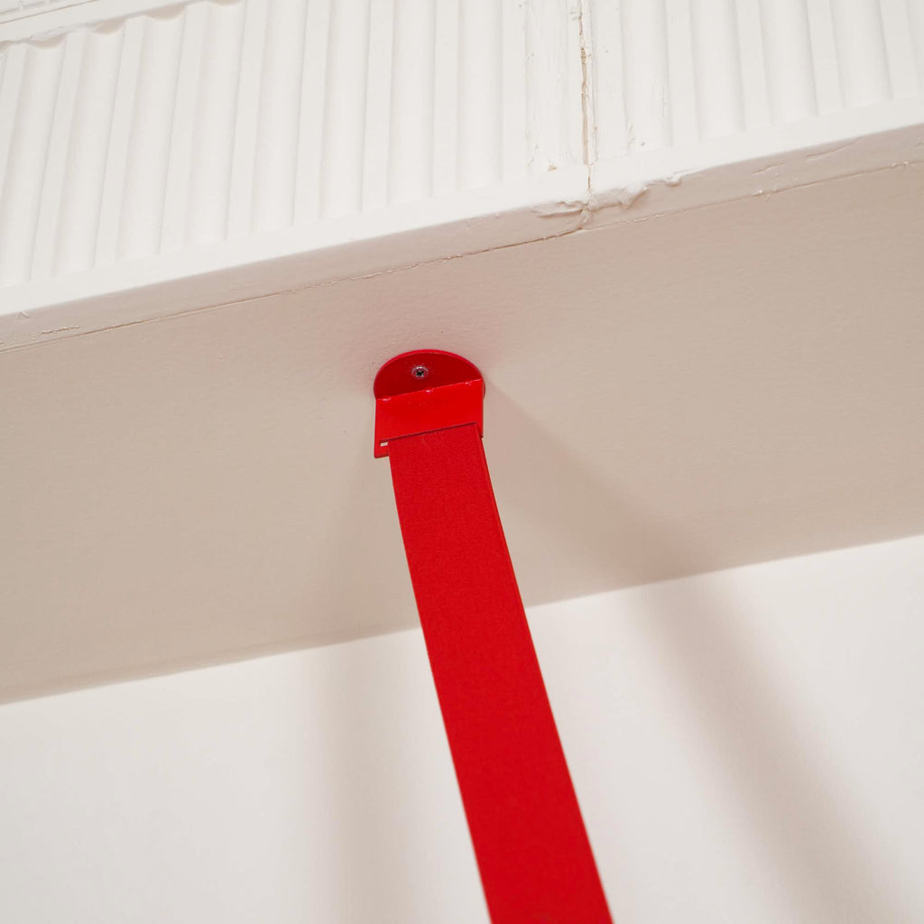 A small red metal plate fixes the top of this Clérachic floor lamp strip to the underside of a white ceiling beam.