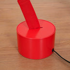 Close view of a red round base on a wood floor, with the Clérachic floor lamp strip rising from a slot and a black cord at the side.