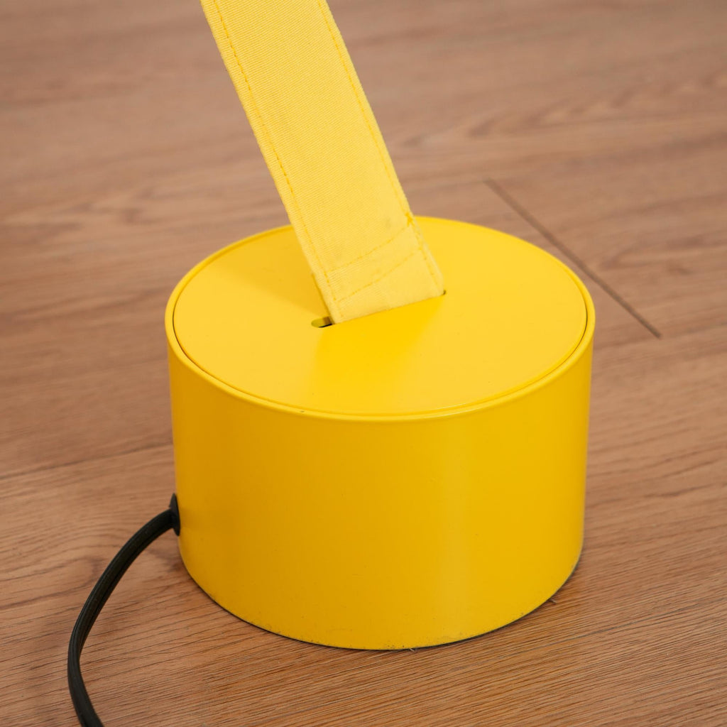 Close view of a yellow round base on a wood floor, with the Clérachic floor lamp strip rising from its slot and a black cord beside it.