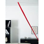 The top of a red Clérachic floor lamp strip fixed at the ceiling, with a black shelf unit and a framed drawing beside it.