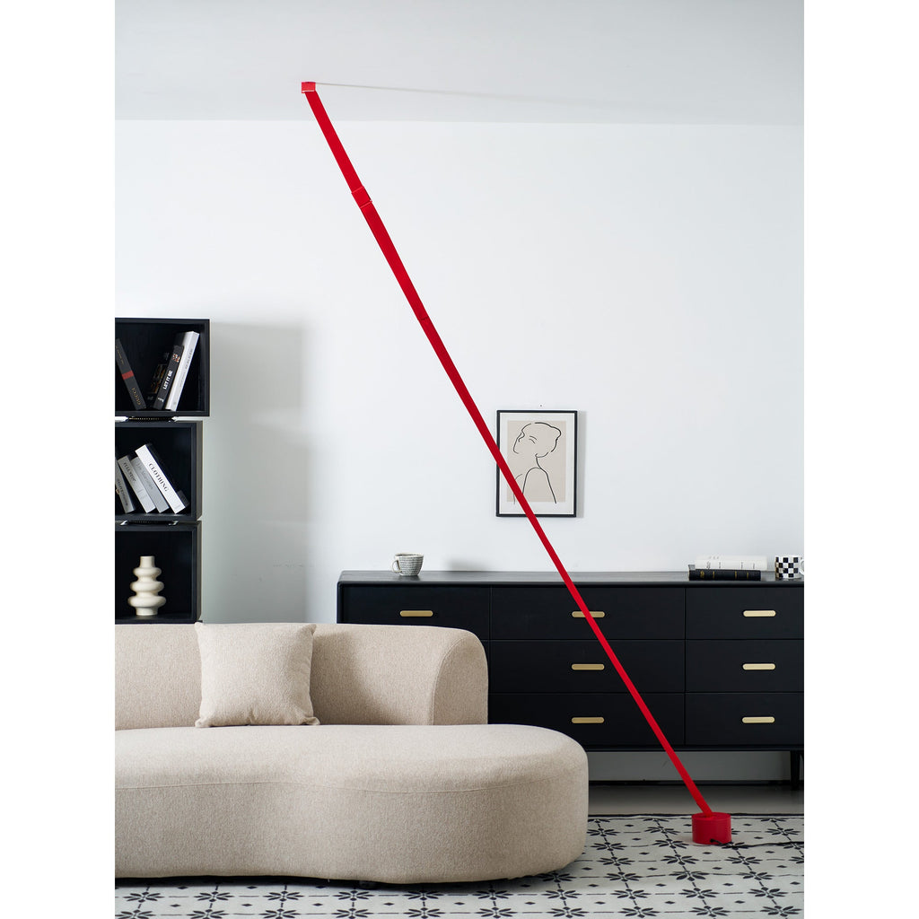 An unlit red Clérachic floor lamp strip leans past a black sideboard with brass handles, with a curved beige sofa in front.