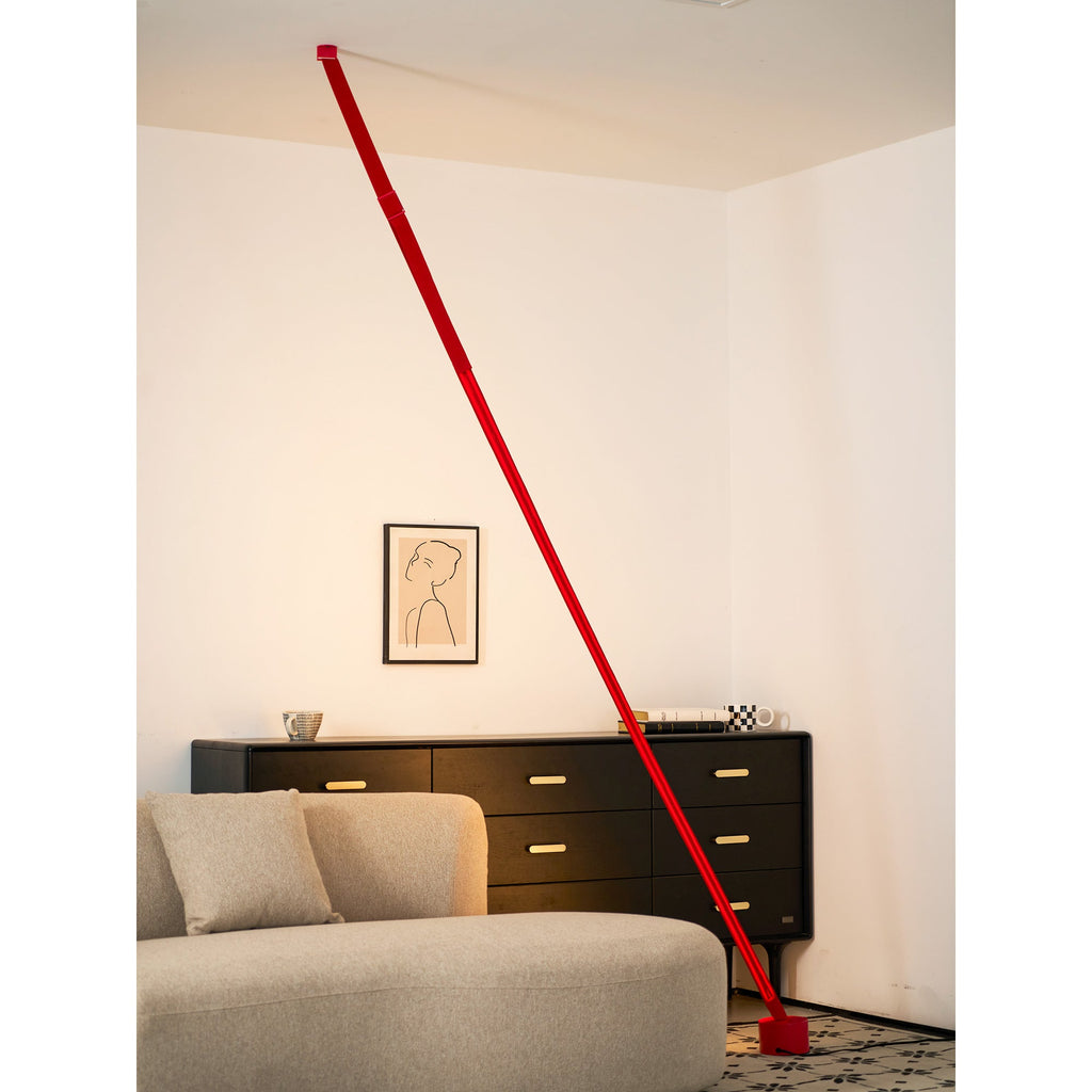 A red Clérachic floor lamp strip leans across a warmly lit corner, with a framed portrait drawing above a black sideboard.