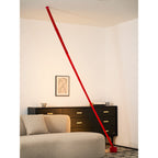 A red Clérachic floor lamp strip leans across a warmly lit corner, with a framed portrait drawing above a black sideboard.