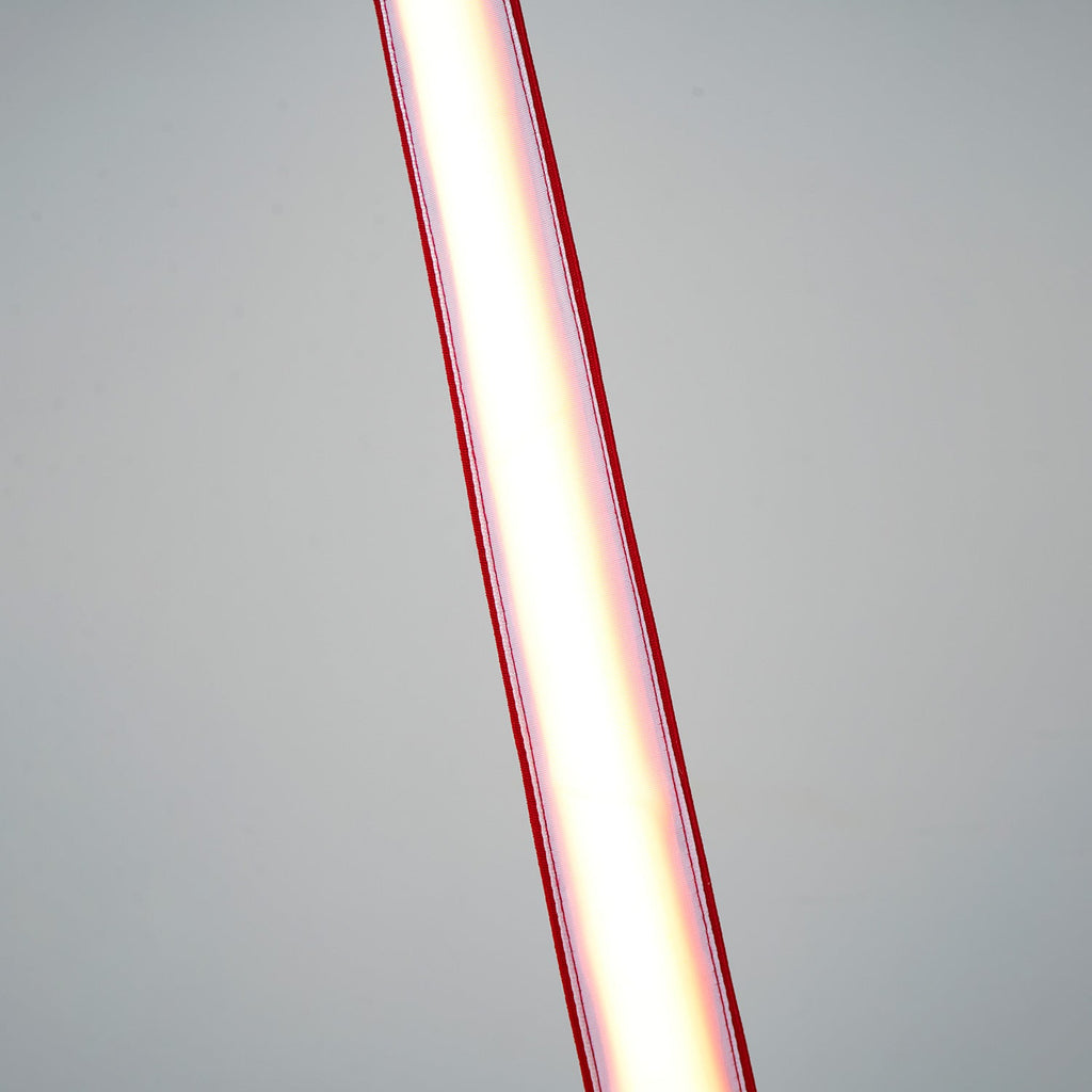 Close view of the lit lower length of this Clérachic floor lamp, the light glowing white inside red edges against a grey backdrop.