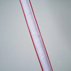 Close view of an unlit Clérachic floor lamp strip, showing the white inner diffuser behind its red edges, on a grey backdrop.