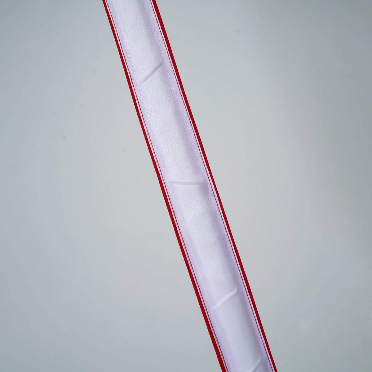 Close view of an unlit Clérachic floor lamp strip, showing the white inner diffuser behind its red edges, on a grey backdrop.