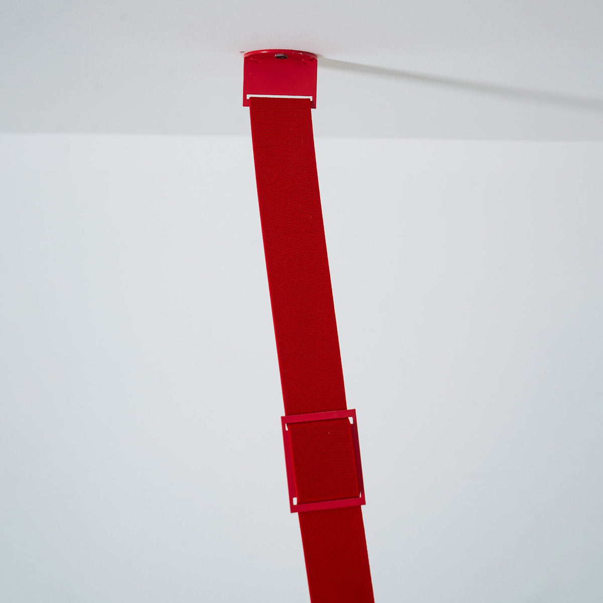 The top of a red Clérachic floor lamp strip meets a white ceiling at a small fixing plate, with a metal sleeve lower down.