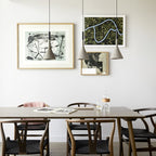 Three Clérachic cone pendants in grey hang at different heights above a wooden dining table, beside framed prints on a white wall.