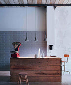 The same three Clérachic cone pendants over a timber counter and brick-tile wall, shown in cooler daylight with a red scale beside them.