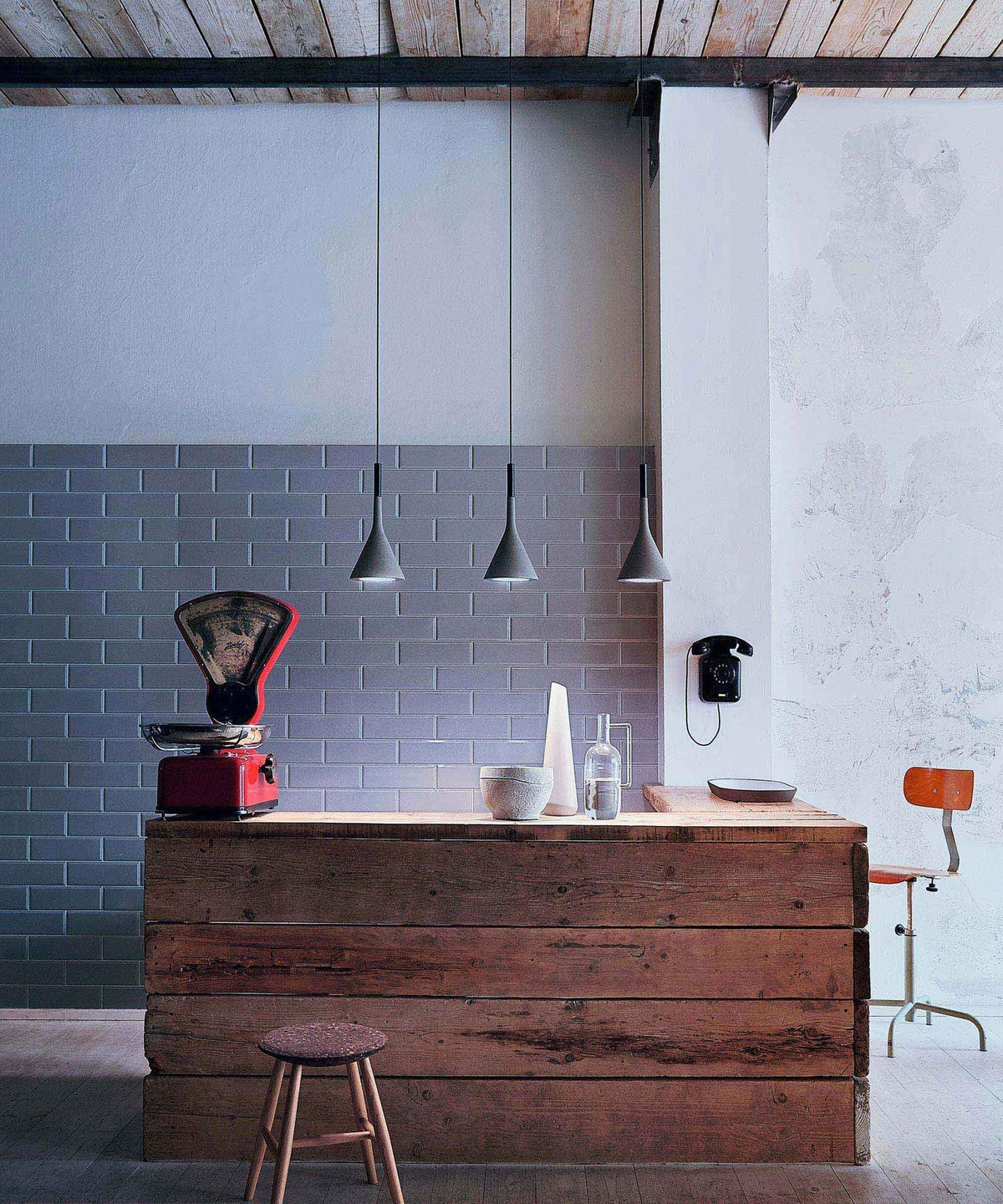 The same three Clérachic cone pendants over a timber counter and brick-tile wall, shown in cooler daylight with a red scale beside them.