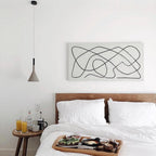 A single grey Clérachic cone pendant hung over a bed with white linen, beside a line-drawing canvas on a white wall.