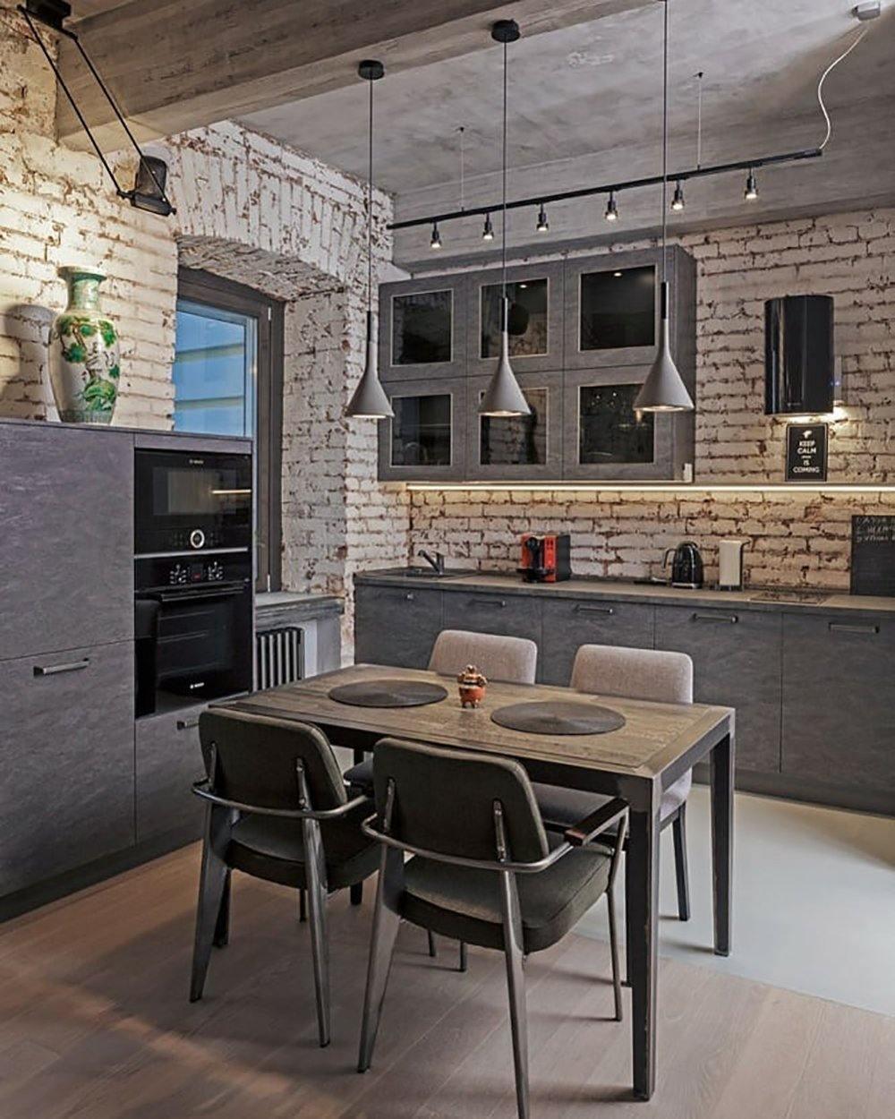 Three Clérachic cone pendants over a table in a loft kitchen with exposed brick walls, a track of spotlights and grey chairs.