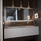 Three Clérachic cone pendants hung in a row above a mirror and a floating white vanity in a dark brown bathroom.