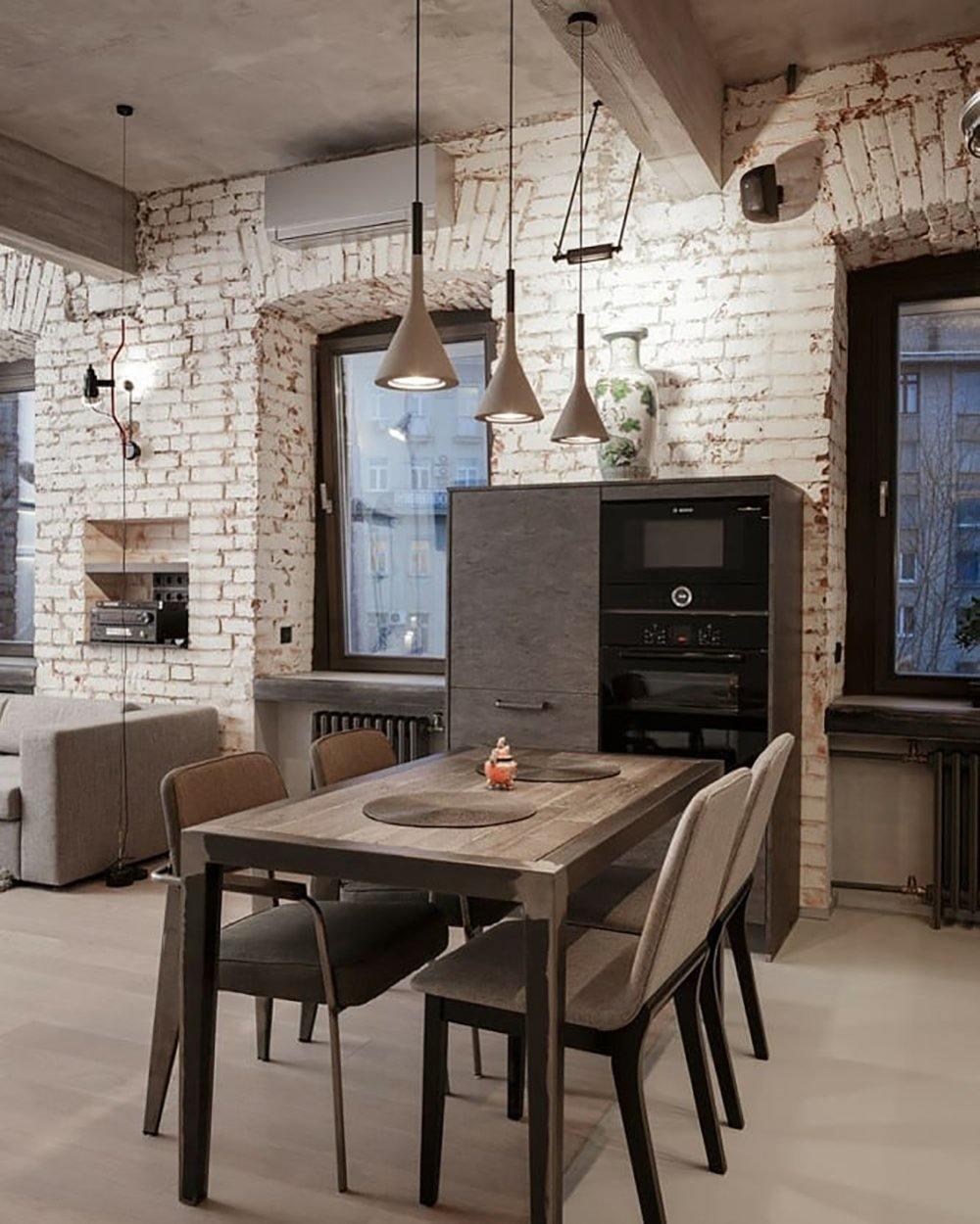 Grey Clérachic cone pendants hung at different heights in an industrial kitchen with white-painted brick and a wooden table.