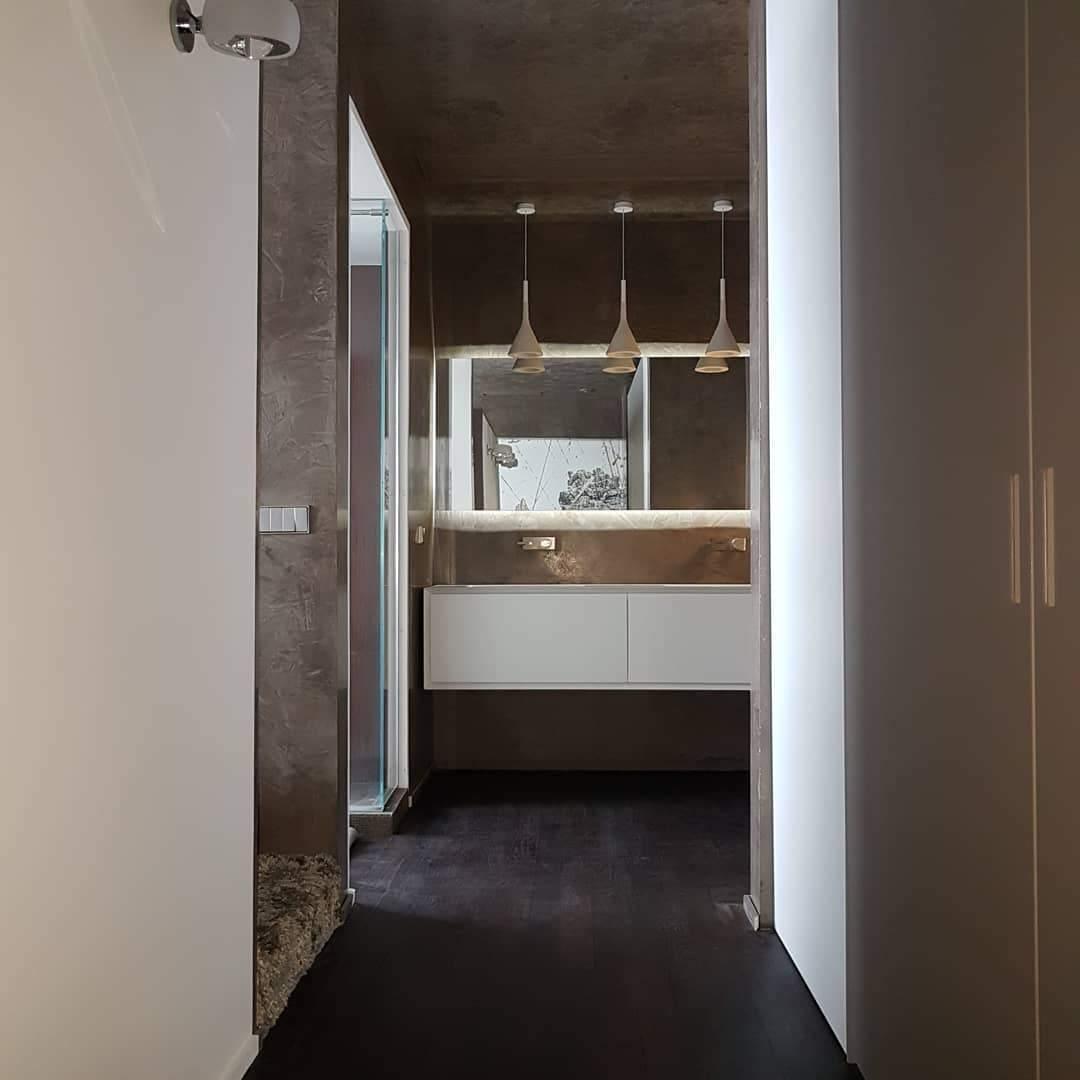 Three Clérachic cone pendants hung in a row over a mirror and white wall-hung vanity in a dark corridor bathroom.