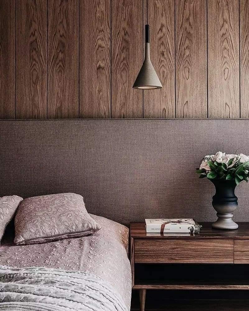 A single grey Clérachic cone pendant against a wood-panelled wall, above a bed with soft mauve bedding and a bedside table.