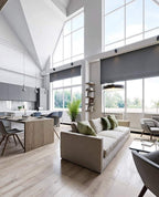Slim grey Clérachic cone pendants hanging in a tall, bright open-plan room with big windows, a sofa and a long kitchen counter.