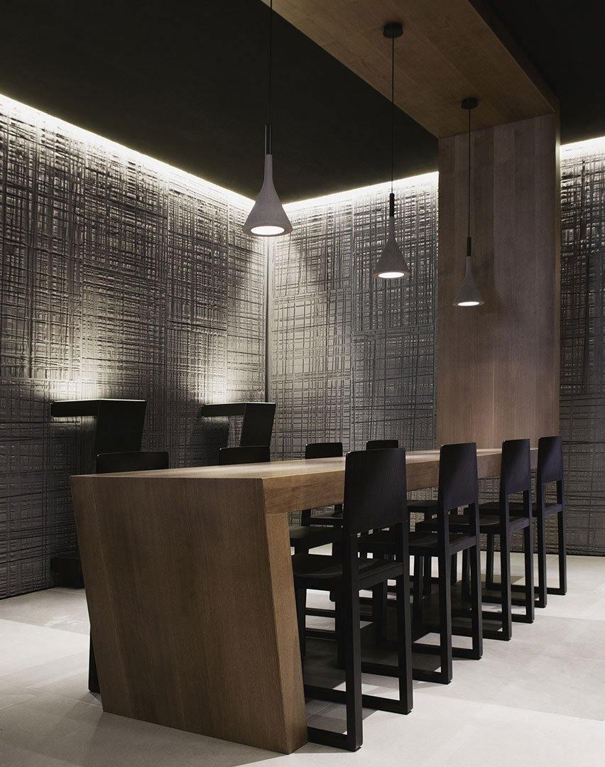 Two Clérachic cone pendants lit in a dark dining room with a textured grey wall, a wooden table and black chairs.