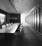 A long row of Clérachic cone pendants above a very long table in a black-and-white room with grey chairs and a bare concrete ceiling.