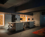 Clérachic cone pendants in a row above steel-framed counters in a dark room with amber light panels in the wall.