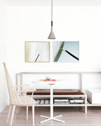 A single grey Clérachic cone pendant over a round white pedestal table, with two framed prints on a white wall and a bench seat.