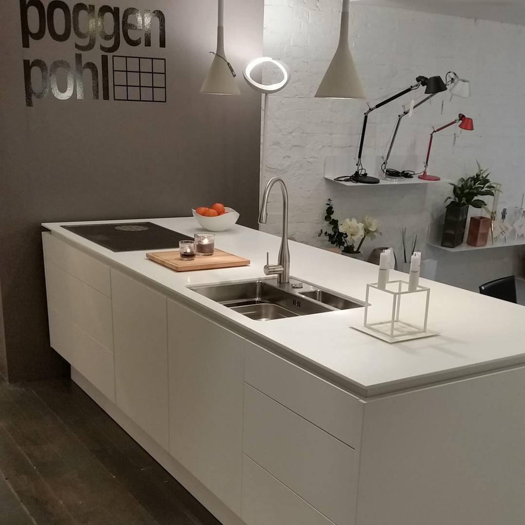 Two Clérachic cone pendants in grey over a kitchen island with a double sink and an angled desk lamp, in front of a white-brick wall.