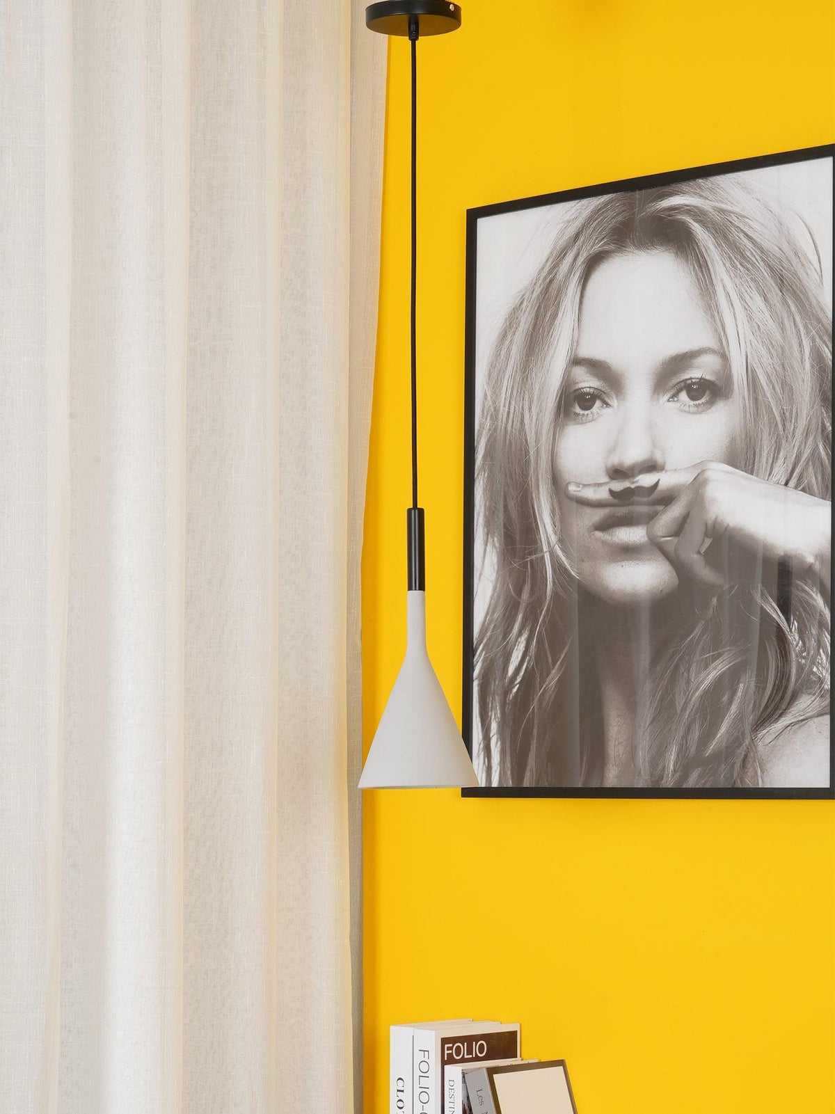 One white Clérachic cone pendant hung in front of a cream curtain and a yellow wall, beside a large black-and-white portrait.