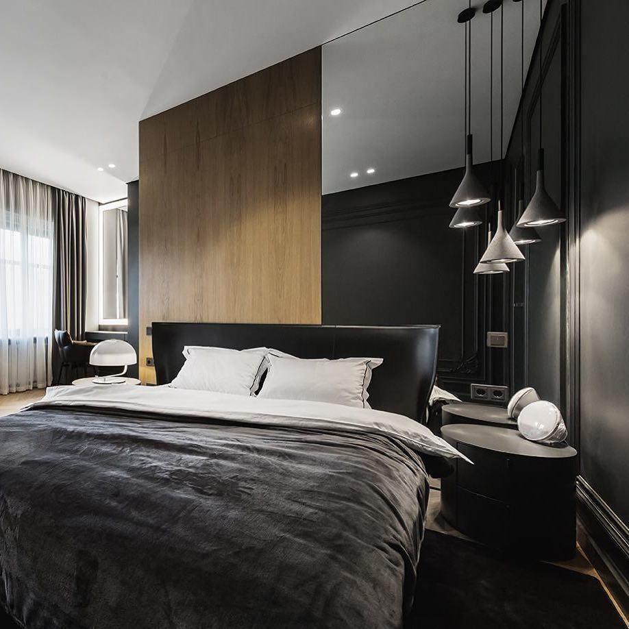 Four Clérachic cone pendants in black and grey over the foot of a bed in a dark bedroom with a wood panel behind the headboard.