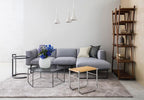 Three white Clérachic cone pendants hung together over a corner sofa in a calm grey living room, beside a tall wooden shelf.