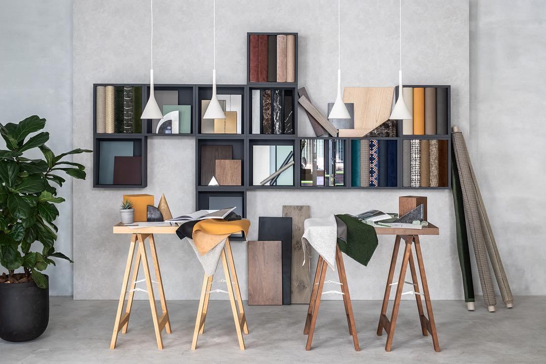 Four small white Clérachic cone pendants hung at different heights above a wall of shelving and two trestle desks with material samples.