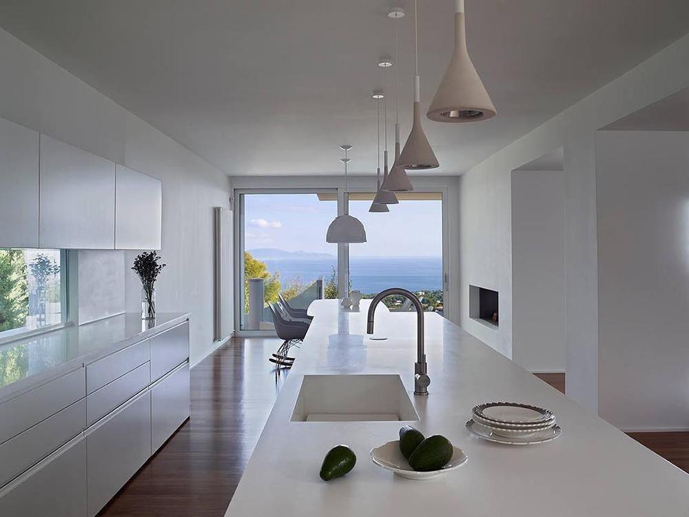 Clérachic cone pendants hung at different heights along a long white kitchen counter, with a sea view through the window at the far end.