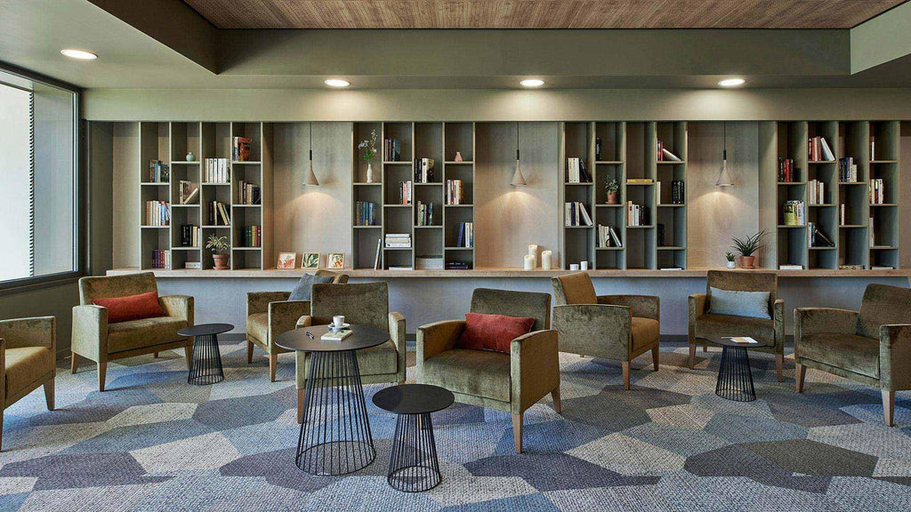 A set of small Clérachic cone pendants lit above reading tables and olive armchairs, in front of a long wall of bookshelves.
