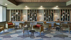 A set of small Clérachic cone pendants lit above reading tables and olive armchairs, in front of a long wall of bookshelves.