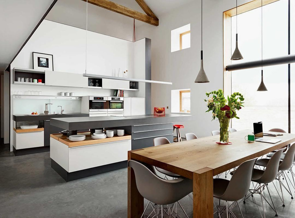 Two Clérachic cone pendants in a loft kitchen with a high timber ceiling, a white island and a long wooden dining table.