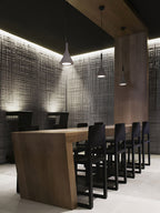 A single Clérachic cone pendant lit above a dark dining table with black chairs, in front of a textured grey wall.