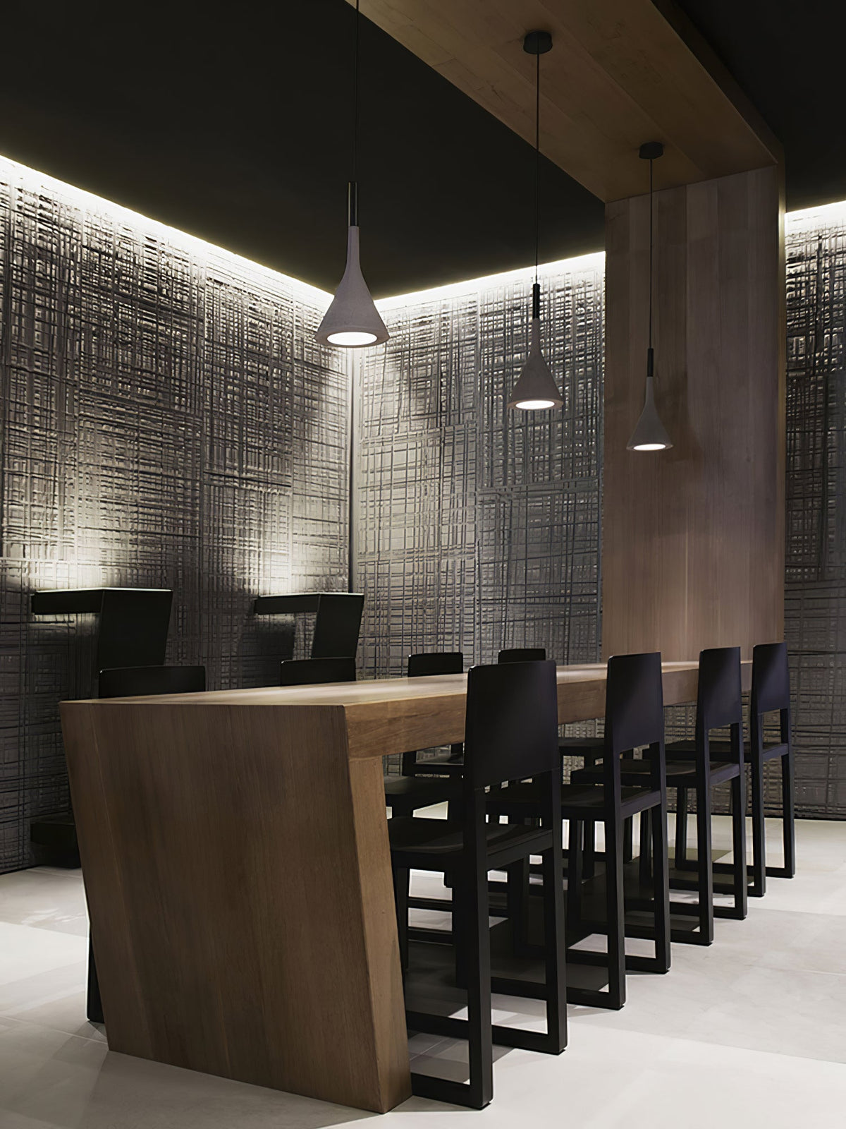 A single Clérachic cone pendant lit above a dark dining table with black chairs, in front of a textured grey wall.