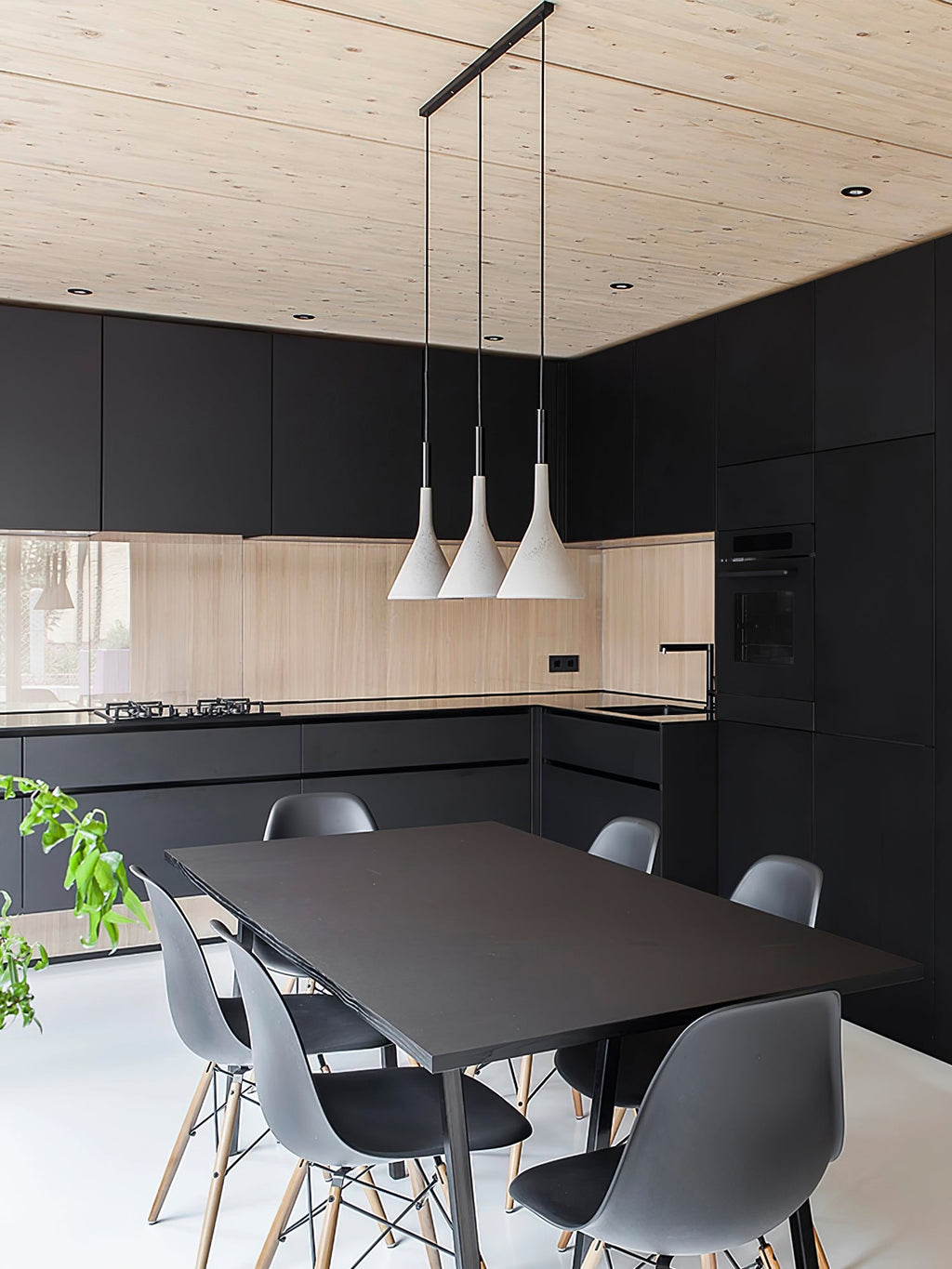 Three white Clérachic cone pendants on a long black bar above a black kitchen table, with grey chairs and a light wood ceiling.