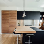 Two light grey Clérachic cone pendants above a kitchen island with a dark worktop, wooden cabinets and a black-faced counter.
