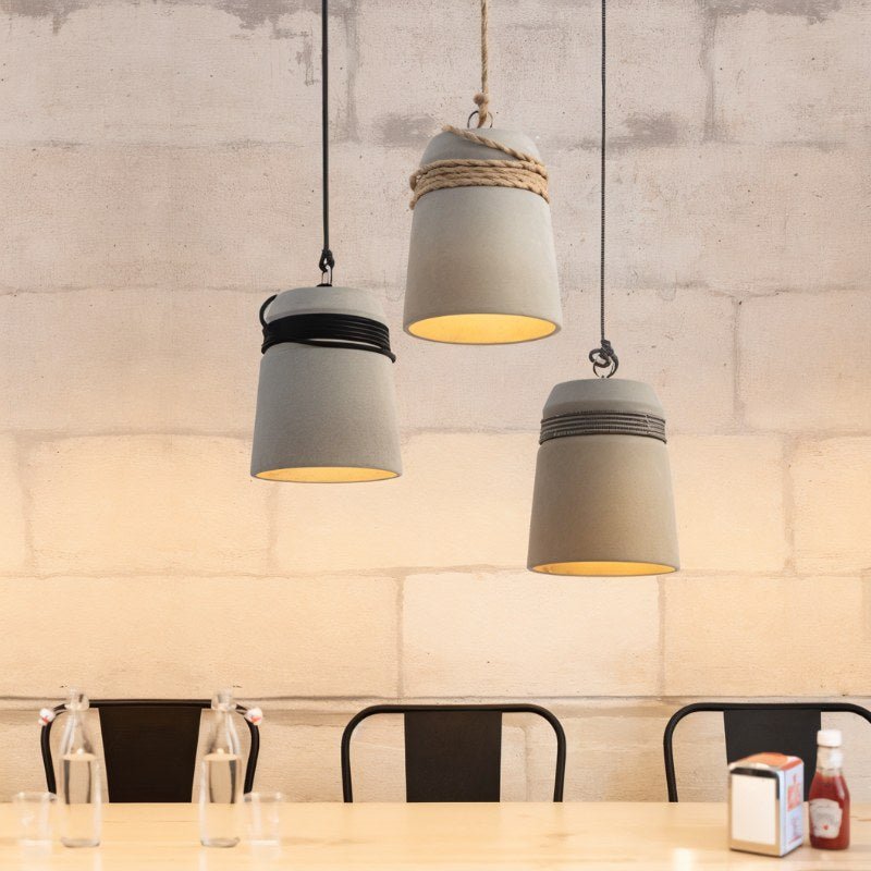 Clérachic three grey concrete bucket pendants in black, hemp and black-and-white rope, glowing warm above a pale wooden table.
