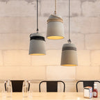 Clérachic three grey concrete bucket pendants in black, hemp and black-and-white rope, glowing warm above a pale wooden table.