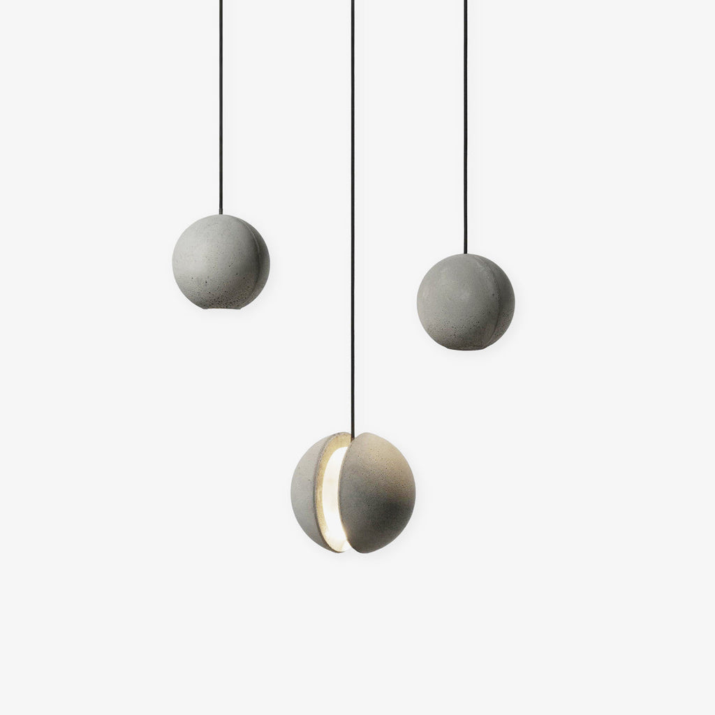 Three Clérachic concrete sphere pendants on black cords against white, two plain and one with a glowing crescent slot.