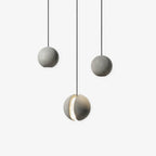 Three Clérachic concrete sphere pendants on black cords against white, two plain and one with a glowing crescent slot.