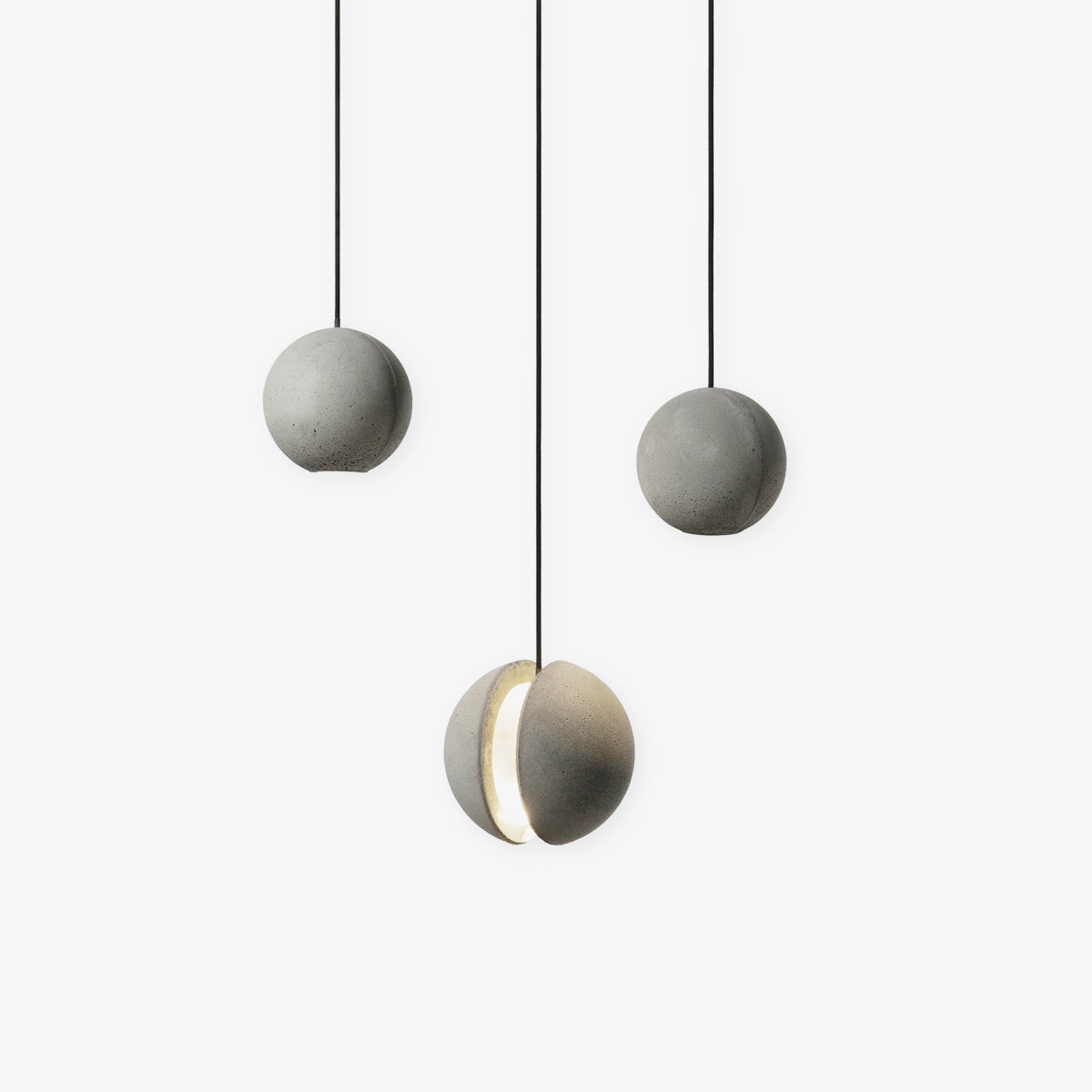 Three Clérachic concrete sphere pendants on black cords against white, two plain and one with a glowing crescent slot.