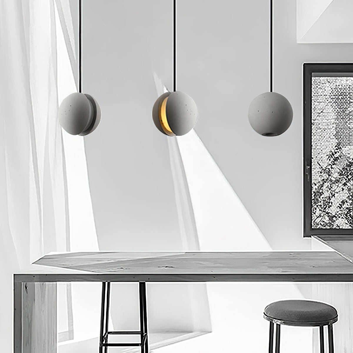 A cement-grey Clérachic sphere pendant with a lit crescent slot hangs between two plain ones above a long table and stool.