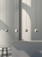 Four Clérachic concrete spheres hang in a row beside a curved plaster wall, alternating plain and slotted, above a concrete counter.