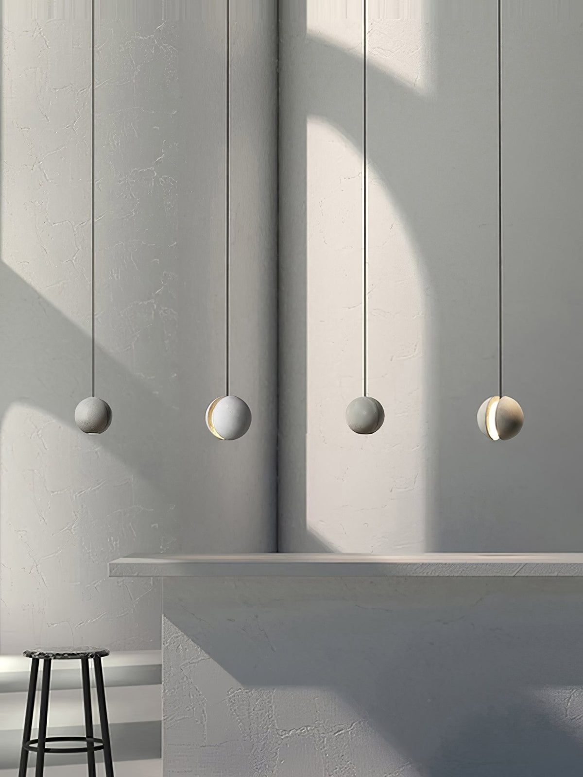 Four Clérachic concrete spheres hang in a row beside a curved plaster wall, alternating plain and slotted, above a concrete counter.